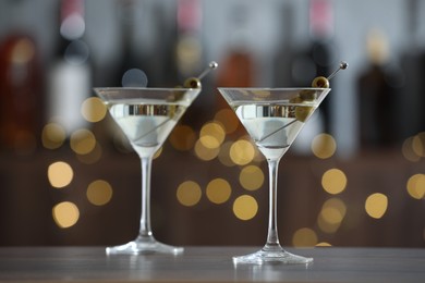 Photo of Martini cocktail with olives in glasses on wooden table against blurred background. Bokeh effect