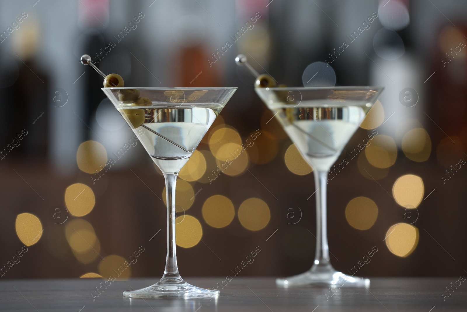 Photo of Martini cocktail with olives in glasses on wooden table against blurred background. Bokeh effect