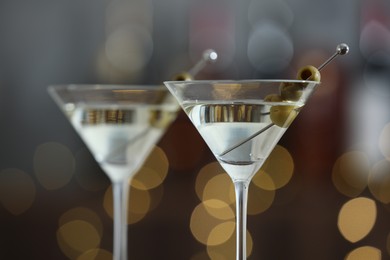 Photo of Martini cocktail with olives in glasses on blurred background, closeup. Bokeh effect