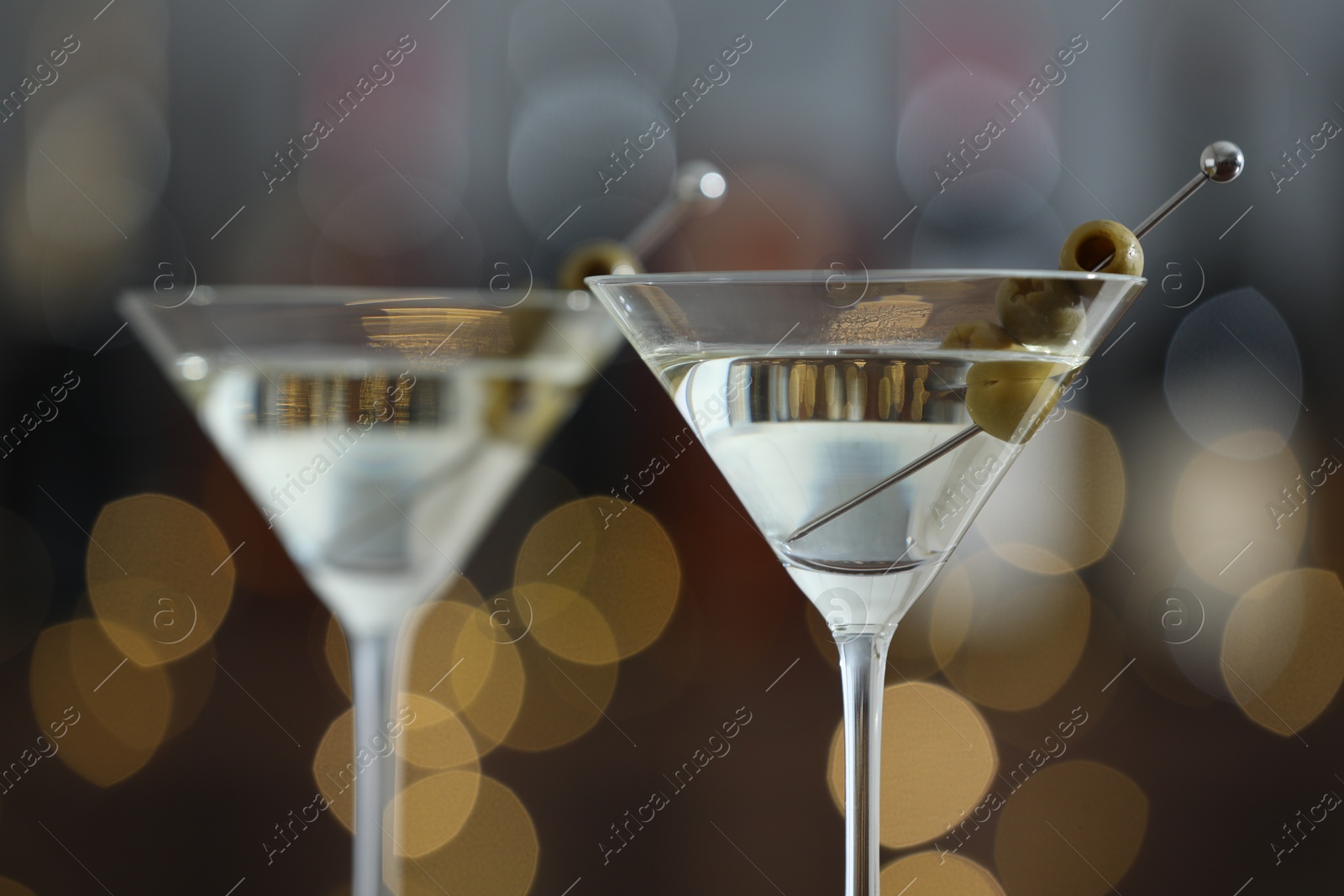 Photo of Martini cocktail with olives in glasses on blurred background, closeup. Bokeh effect