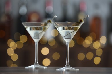 Photo of Martini cocktail with olives in glasses on wooden table against blurred background, closeup. Bokeh effect