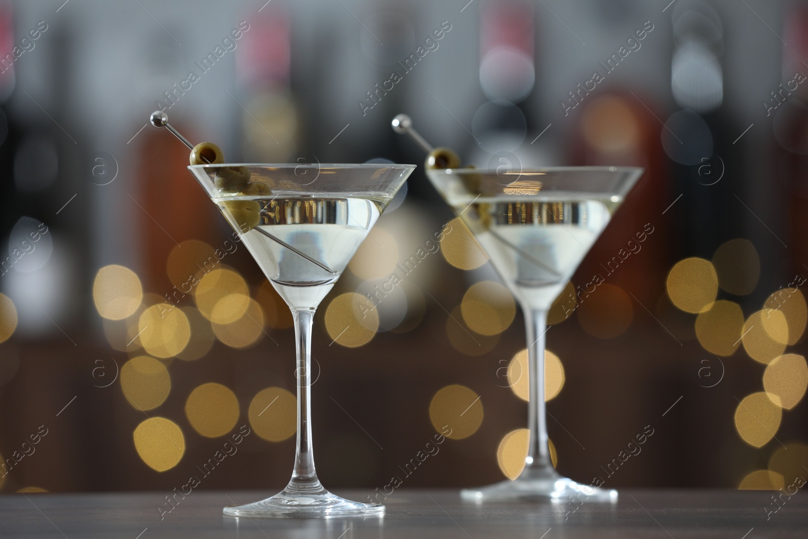 Photo of Martini cocktail with olives in glasses on wooden table against blurred background, closeup. Bokeh effect