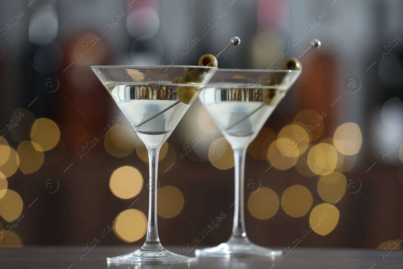 Photo of Martini cocktail with olives in glasses on wooden table against blurred background, closeup. Bokeh effect