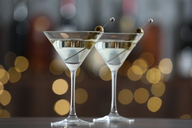 Photo of Martini cocktail with olives in glasses on wooden table against blurred background, closeup. Bokeh effect