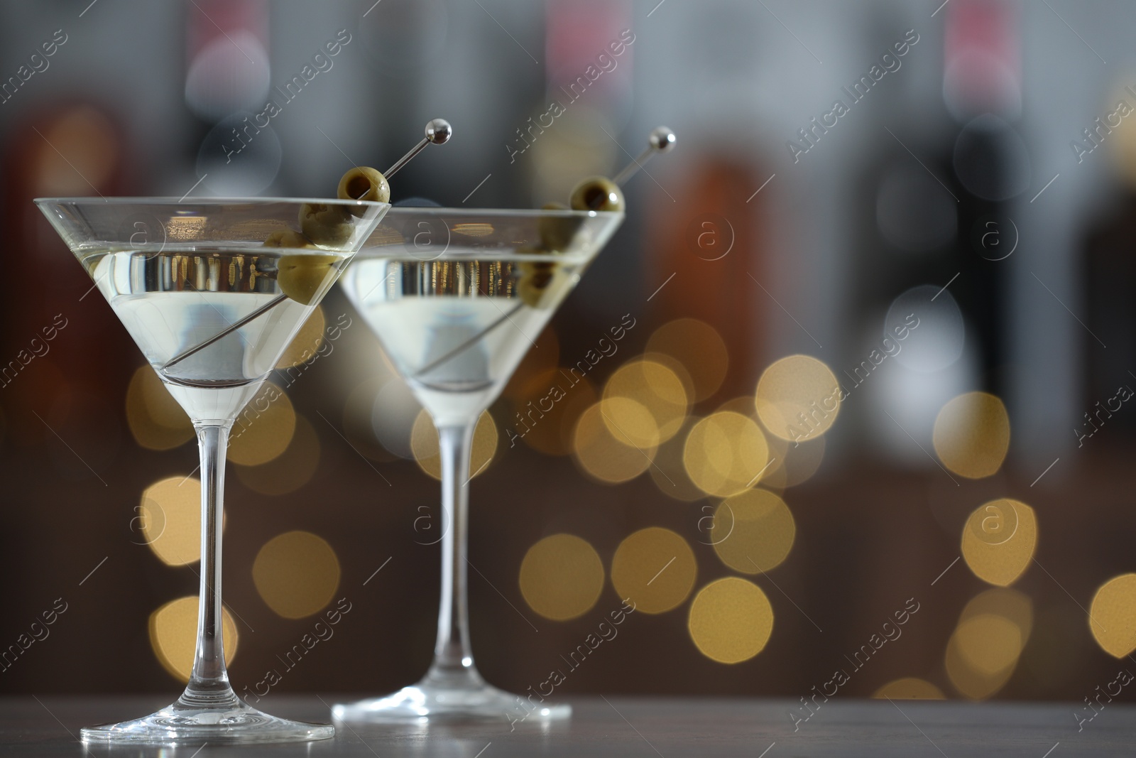 Photo of Martini cocktail with olives in glasses on wooden table against blurred background, closeup. Bokeh effect