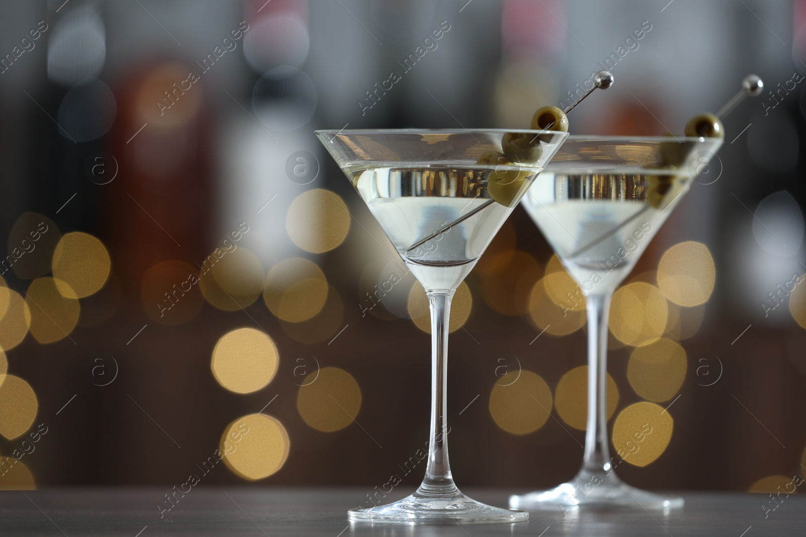 Photo of Martini cocktail with olives in glasses on wooden table against blurred background, closeup. Bokeh effect