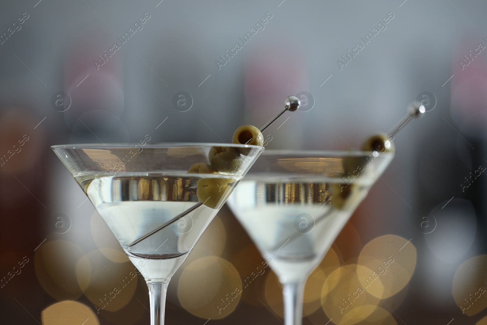 Photo of Martini cocktail with olives in glasses on blurred background, closeup. Bokeh effect