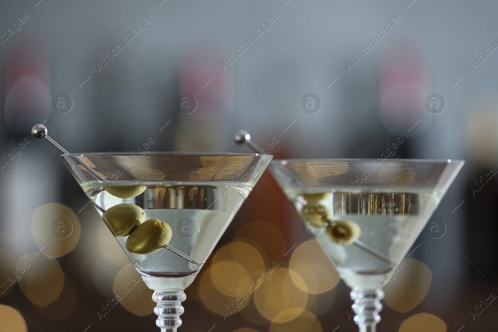 Photo of Martini cocktail with olives in glasses on blurred background, closeup. Bokeh effect