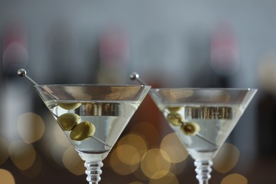 Photo of Martini cocktail with olives in glasses on blurred background, closeup. Bokeh effect