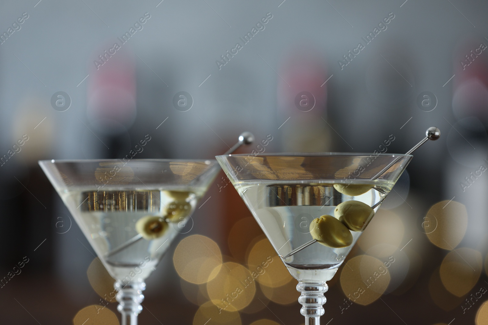 Photo of Martini cocktail with olives in glasses on blurred background, closeup. Bokeh effect