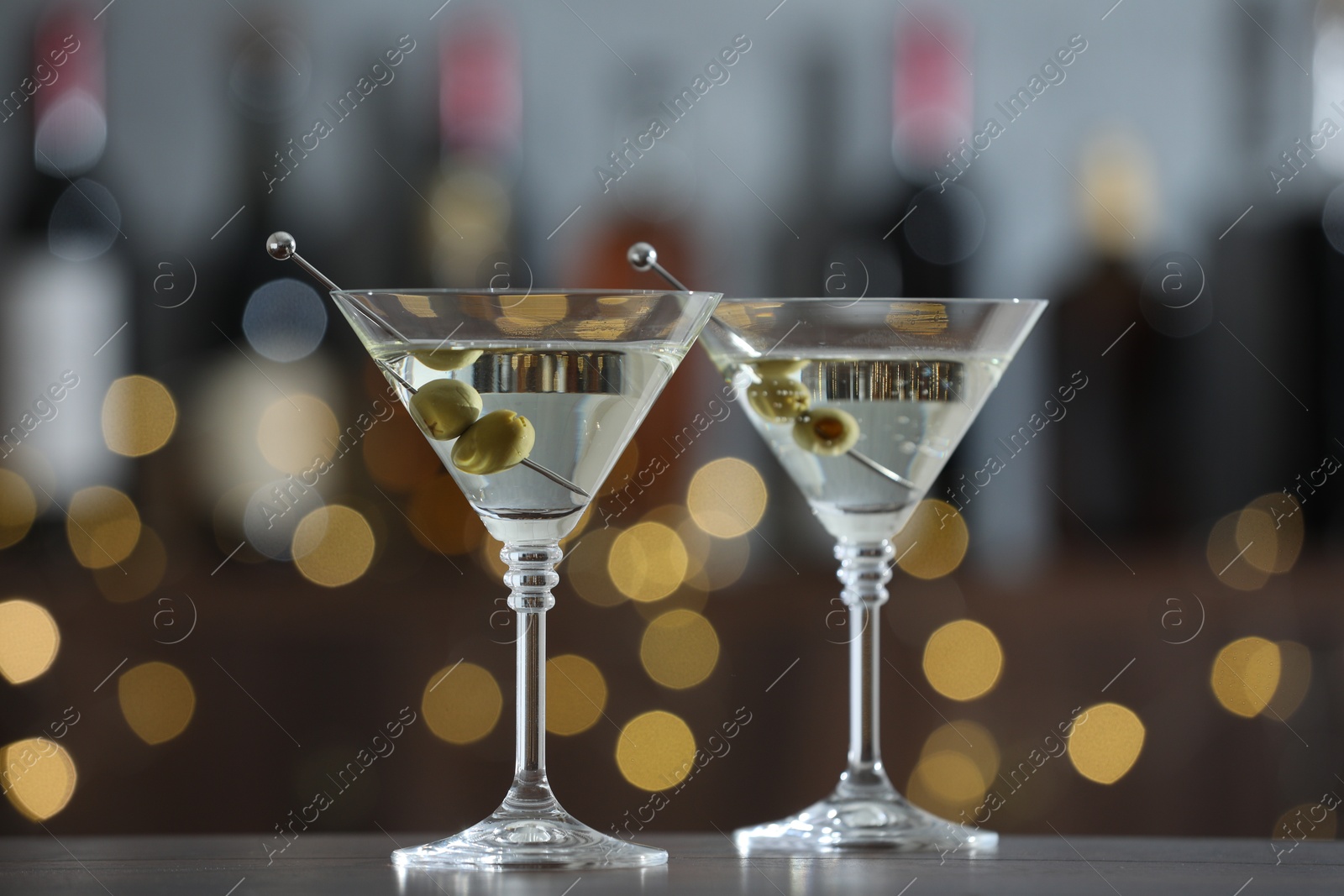 Photo of Martini cocktail with olives in glasses on wooden table against blurred background. Bokeh effect