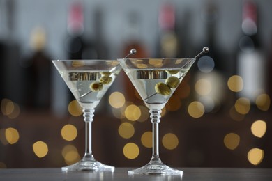 Photo of Martini cocktail with olives in glasses on wooden table against blurred background. Bokeh effect