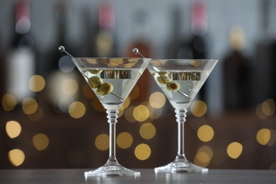 Photo of Martini cocktail with olives in glasses on wooden table against blurred background. Bokeh effect