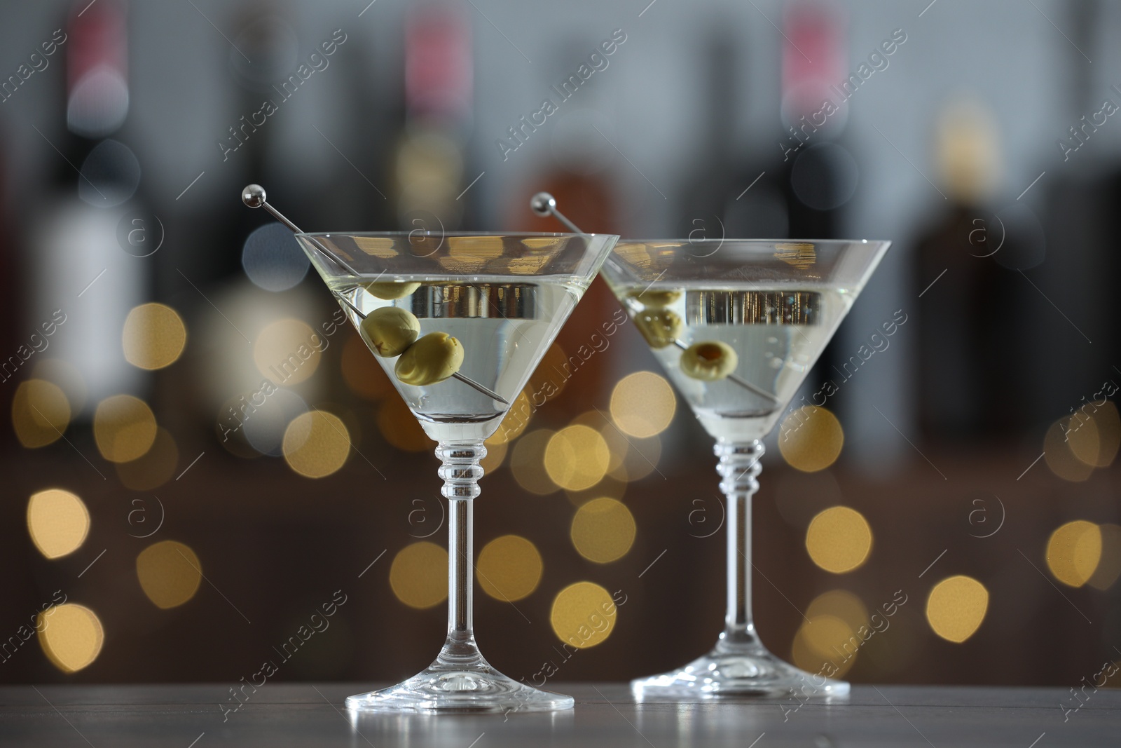 Photo of Martini cocktail with olives in glasses on wooden table against blurred background. Bokeh effect