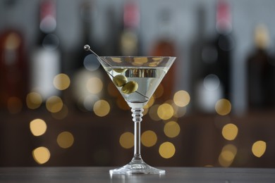 Photo of Martini cocktail with olives in glass on wooden table against blurred background. Bokeh effect