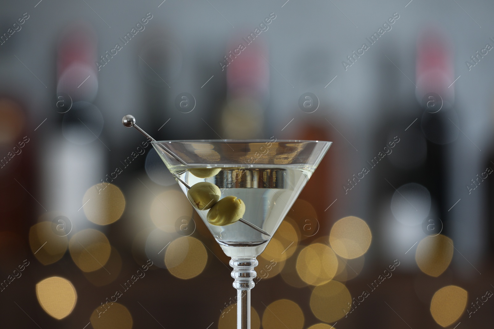 Photo of Martini cocktail with olives in glass on blurred background, closeup. Bokeh effect