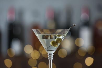 Photo of Martini cocktail with olives in glass on blurred background, closeup. Bokeh effect