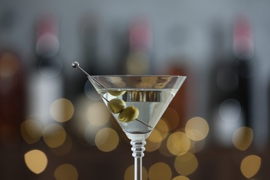 Photo of Martini cocktail with olives in glass on blurred background, closeup. Bokeh effect