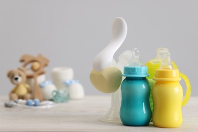 Feeding bottles with milk and breast pump on white wooden table, space for text