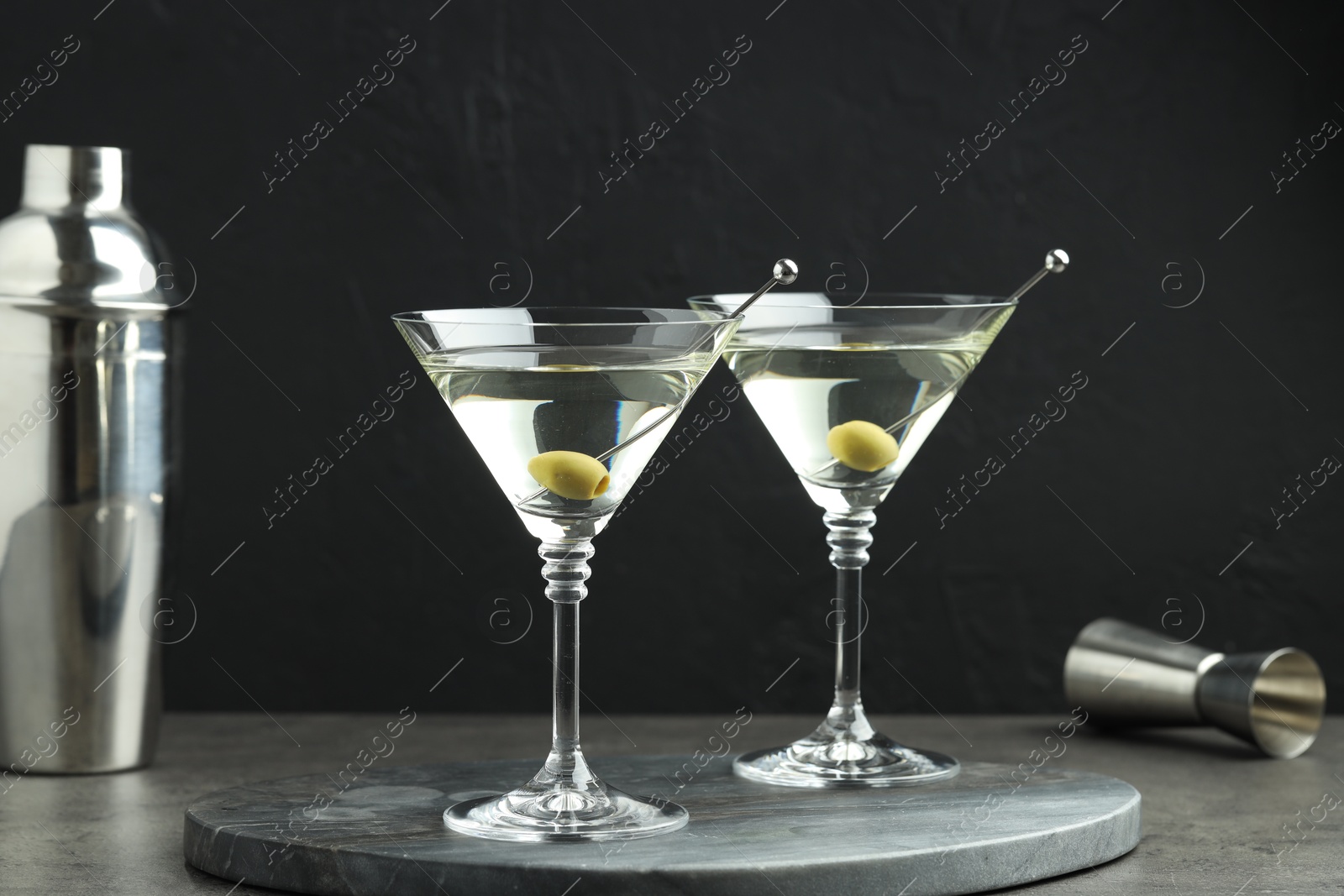 Photo of Martini cocktail with olives in glasses on grey table against black background