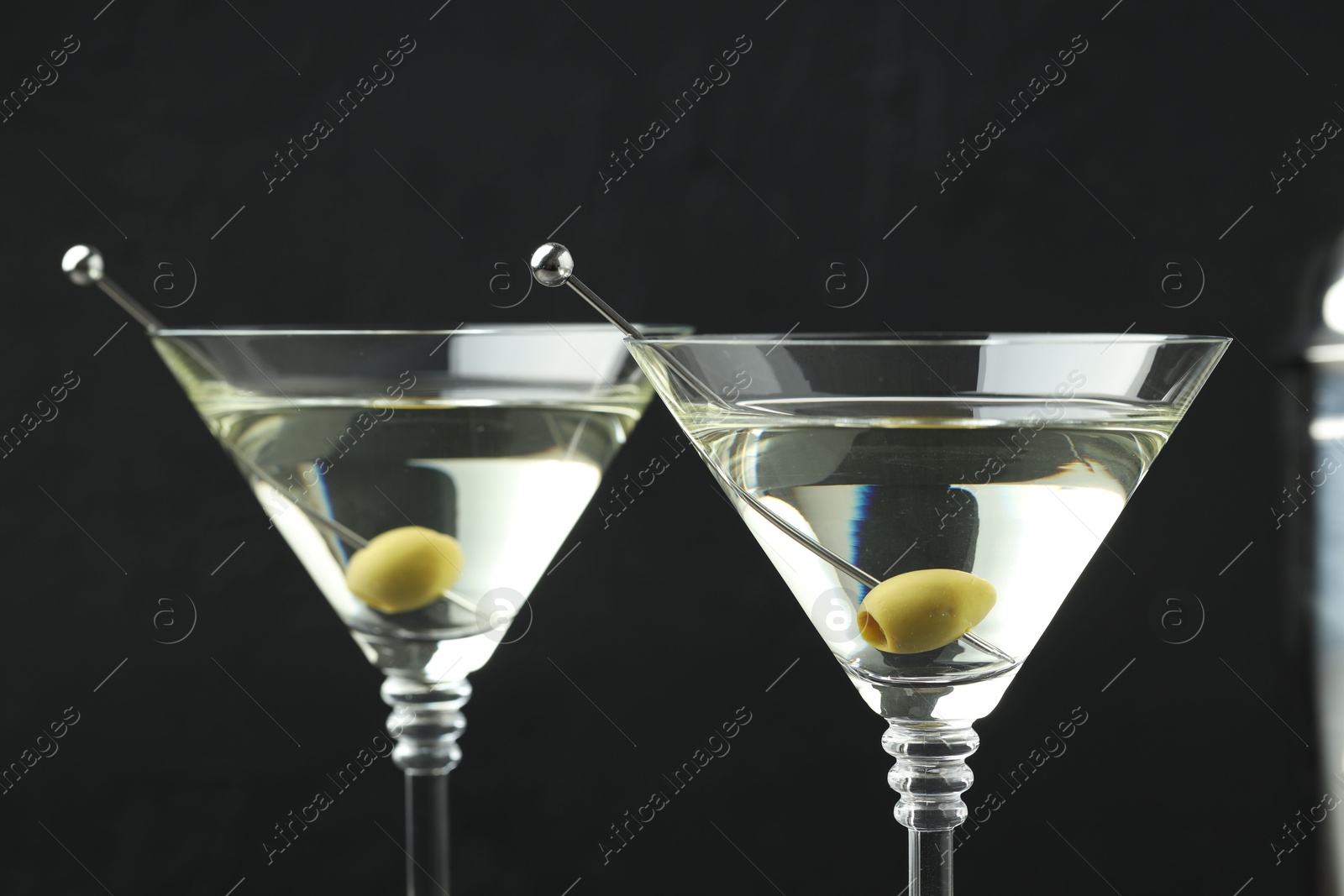 Photo of Martini cocktail with olives in glasses on black background, closeup