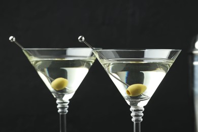 Photo of Martini cocktail with olives in glasses on black background, closeup