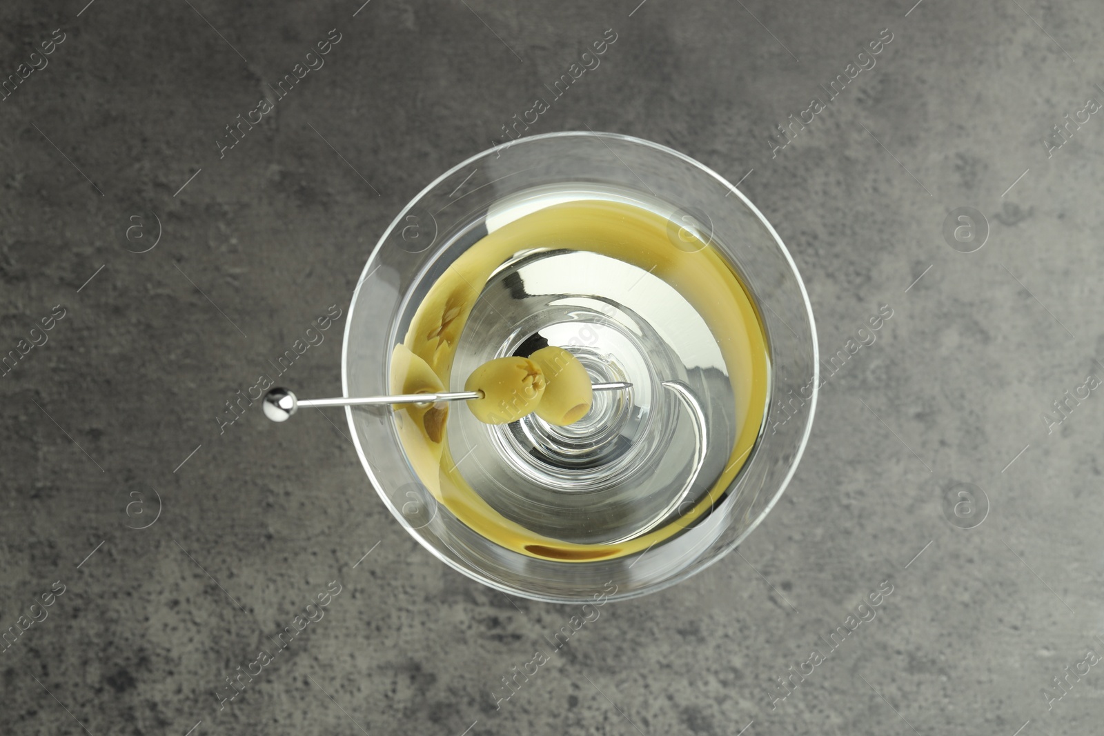 Photo of Martini cocktail with olives in glass on grey table, top view