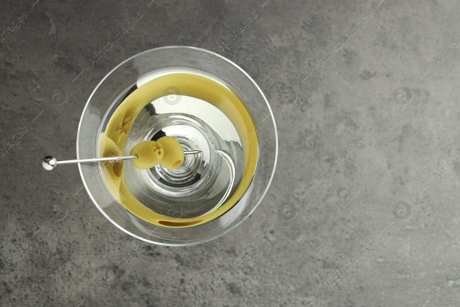 Photo of Martini cocktail with olives in glass on grey table, top view. Space for text