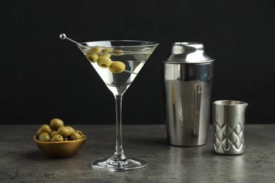 Photo of Martini cocktail with olives in glass and shaker on grey table against black background