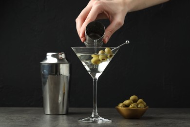 Photo of Woman making martini cocktail with olives on grey table, closeup