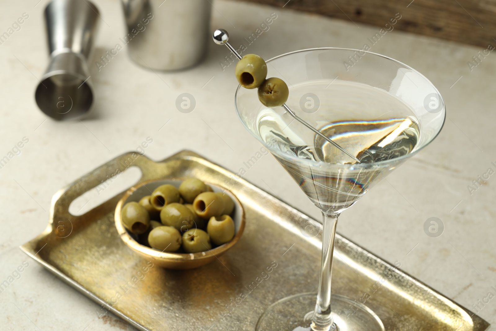 Photo of Martini cocktail with olives in glass and shaker on light table, closeup