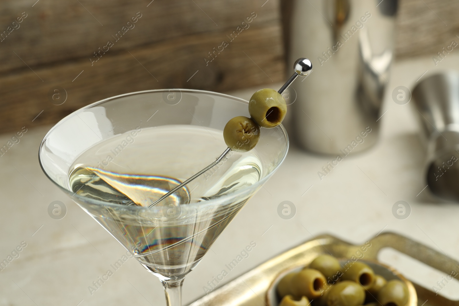 Photo of Martini cocktail with olives in glass and shaker on light table, closeup