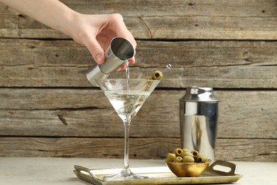 Photo of Woman making martini cocktail with olives on light table, closeup