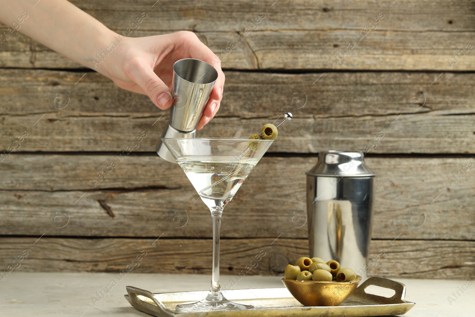 Photo of Woman making tasty martini cocktail with olives at light table, closeup