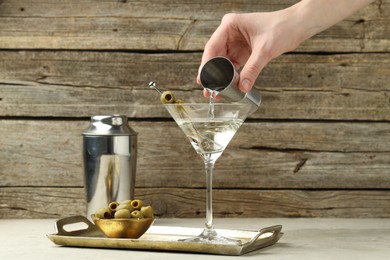 Photo of Woman making martini cocktail with olives on light table, closeup