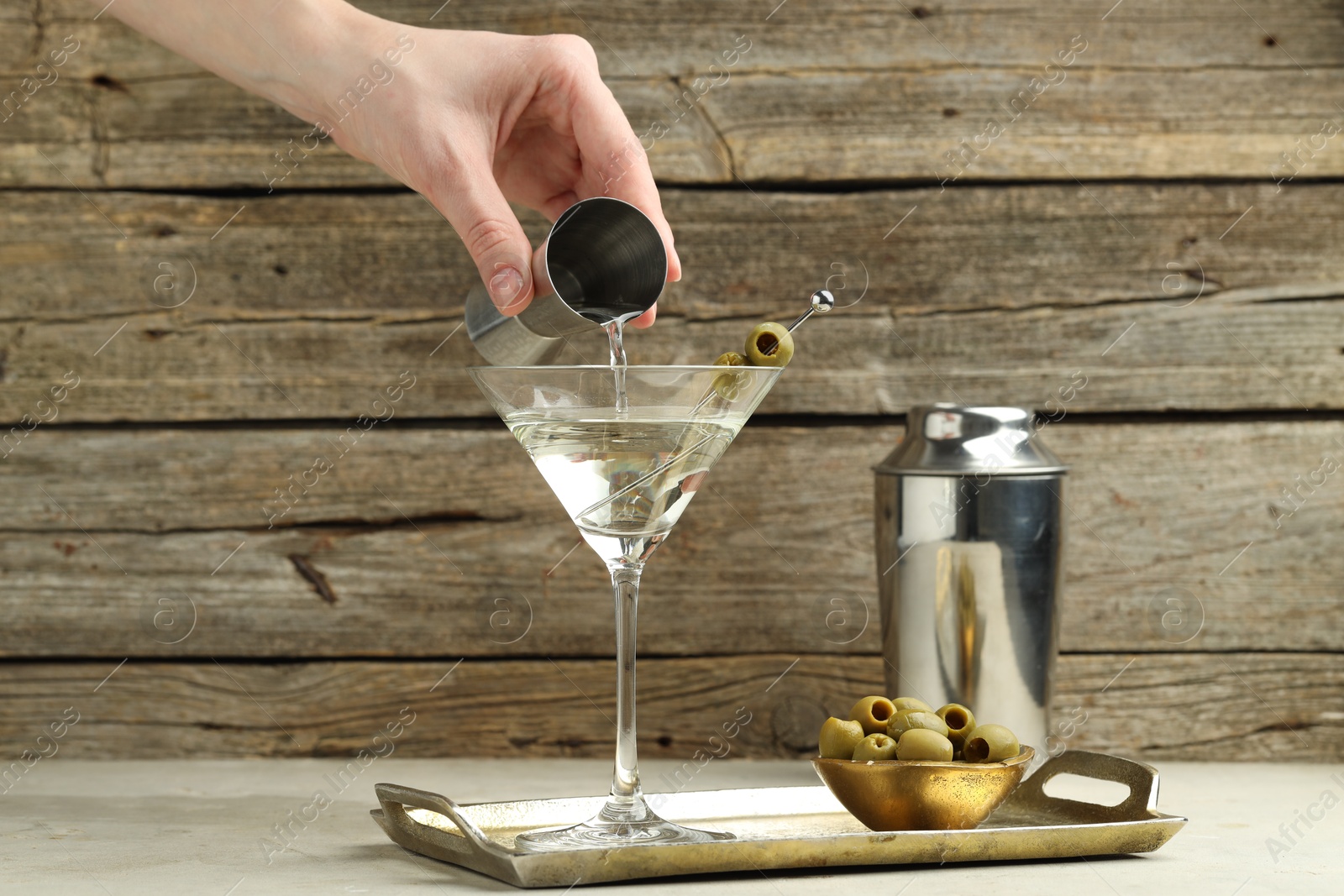 Photo of Woman making martini cocktail with olives on light table, closeup