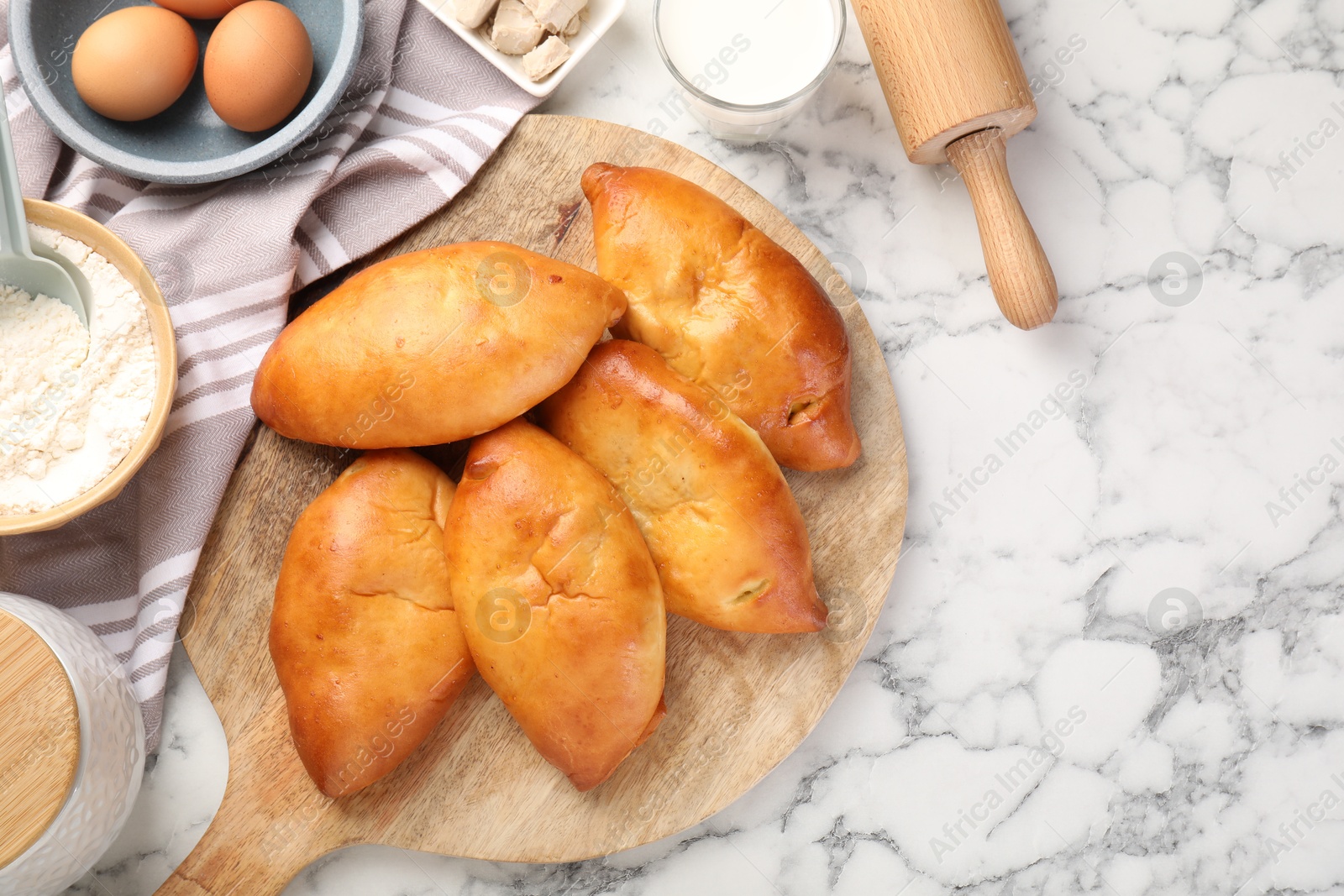 Photo of Delicious pirozhki (stuffed pastry pies) and ingredients on white marble table, flat lay. Space for text