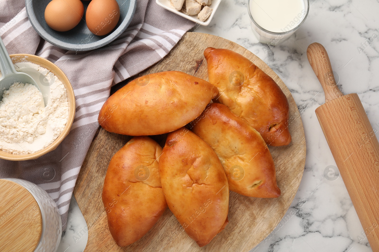 Photo of Delicious pirozhki (stuffed pastry pies) and ingredients on white marble table, flat lay