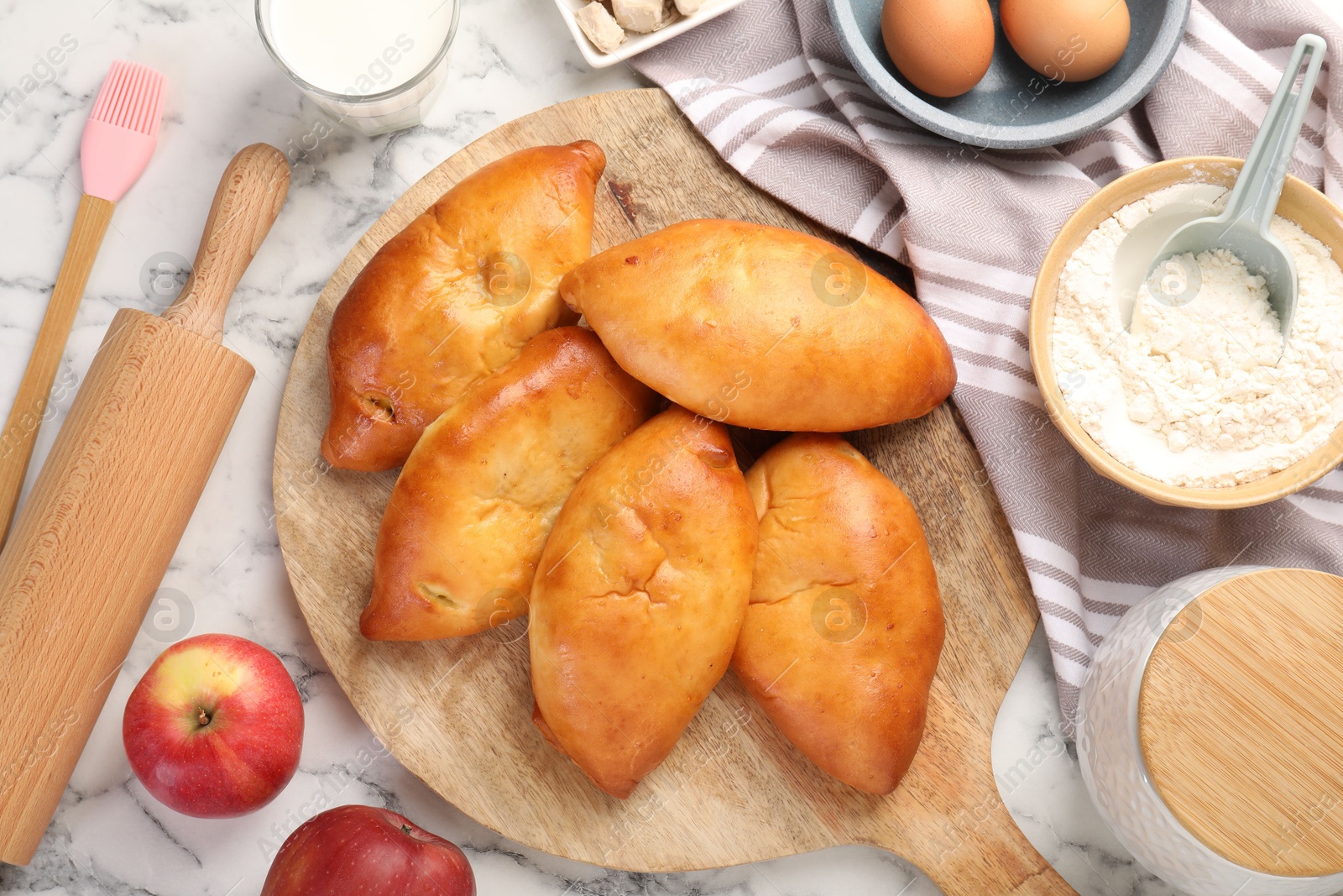 Photo of Delicious pirozhki (stuffed pastry pies) and ingredients on white marble table, flat lay