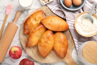 Photo of Delicious pirozhki (stuffed pastry pies) and ingredients on white marble table, flat lay