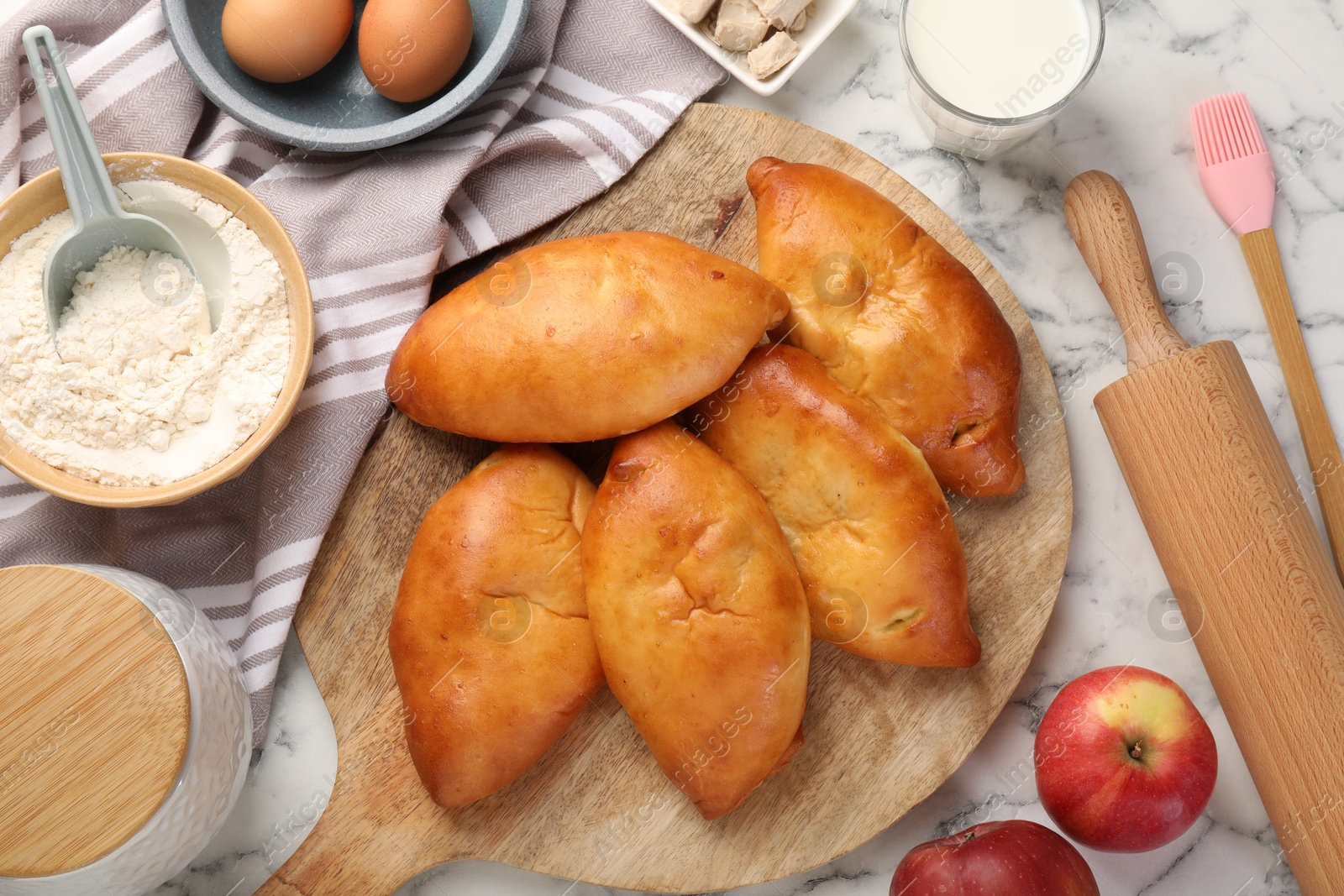 Photo of Delicious pirozhki (stuffed pastry pies) and ingredients on white marble table, flat lay