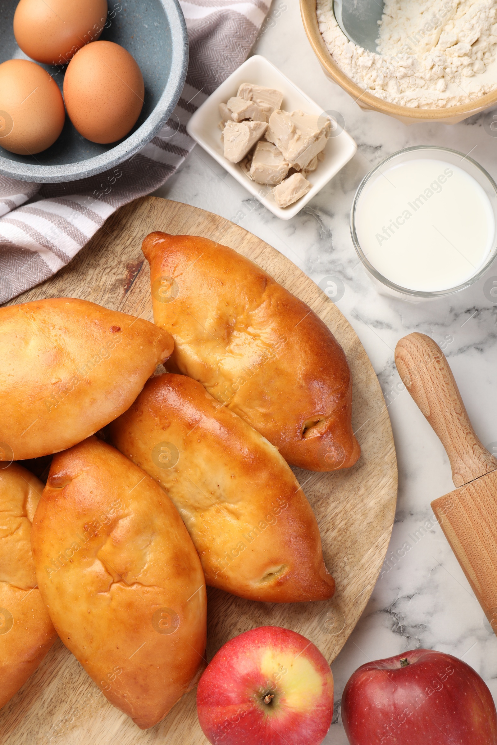 Photo of Delicious pirozhki (stuffed pastry pies) and ingredients on white marble table, flat lay