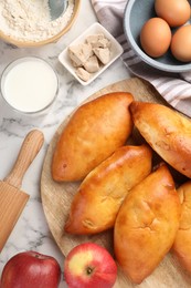 Photo of Delicious pirozhki (stuffed pastry pies) and ingredients on white marble table, flat lay