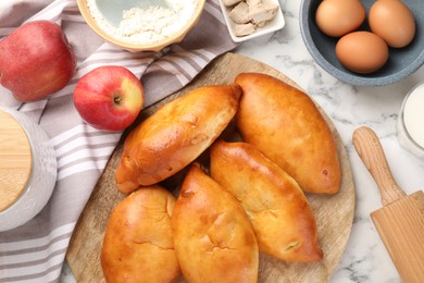 Photo of Delicious pirozhki (stuffed pastry pies) and ingredients on white marble table, flat lay