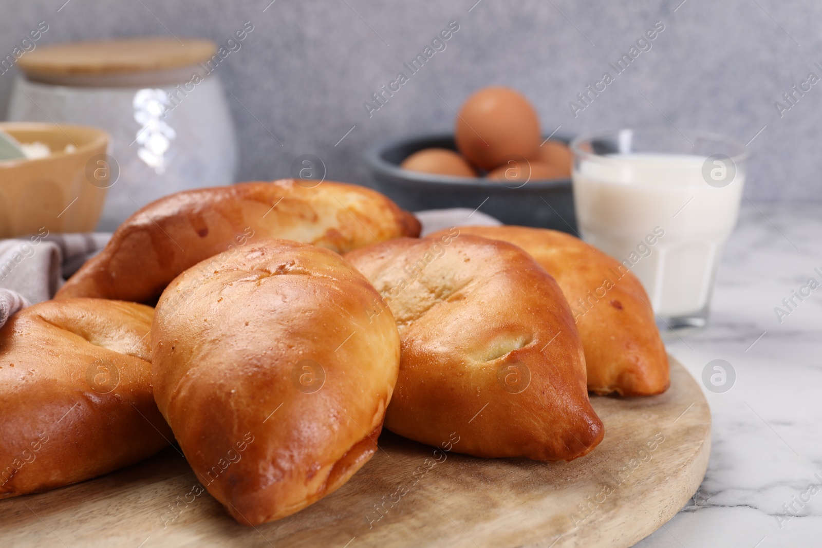 Photo of Delicious pirozhki (stuffed pastry pies) and ingredients on white marble table, closeup