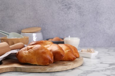 Photo of Delicious pirozhki (stuffed pastry pies) and ingredients on white marble table, closeup. Space for text