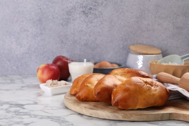 Photo of Delicious pirozhki (stuffed pastry pies) and ingredients on white marble table, closeup. Space for text