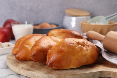 Photo of Delicious pirozhki (stuffed pastry pies) and ingredients on white marble table, closeup