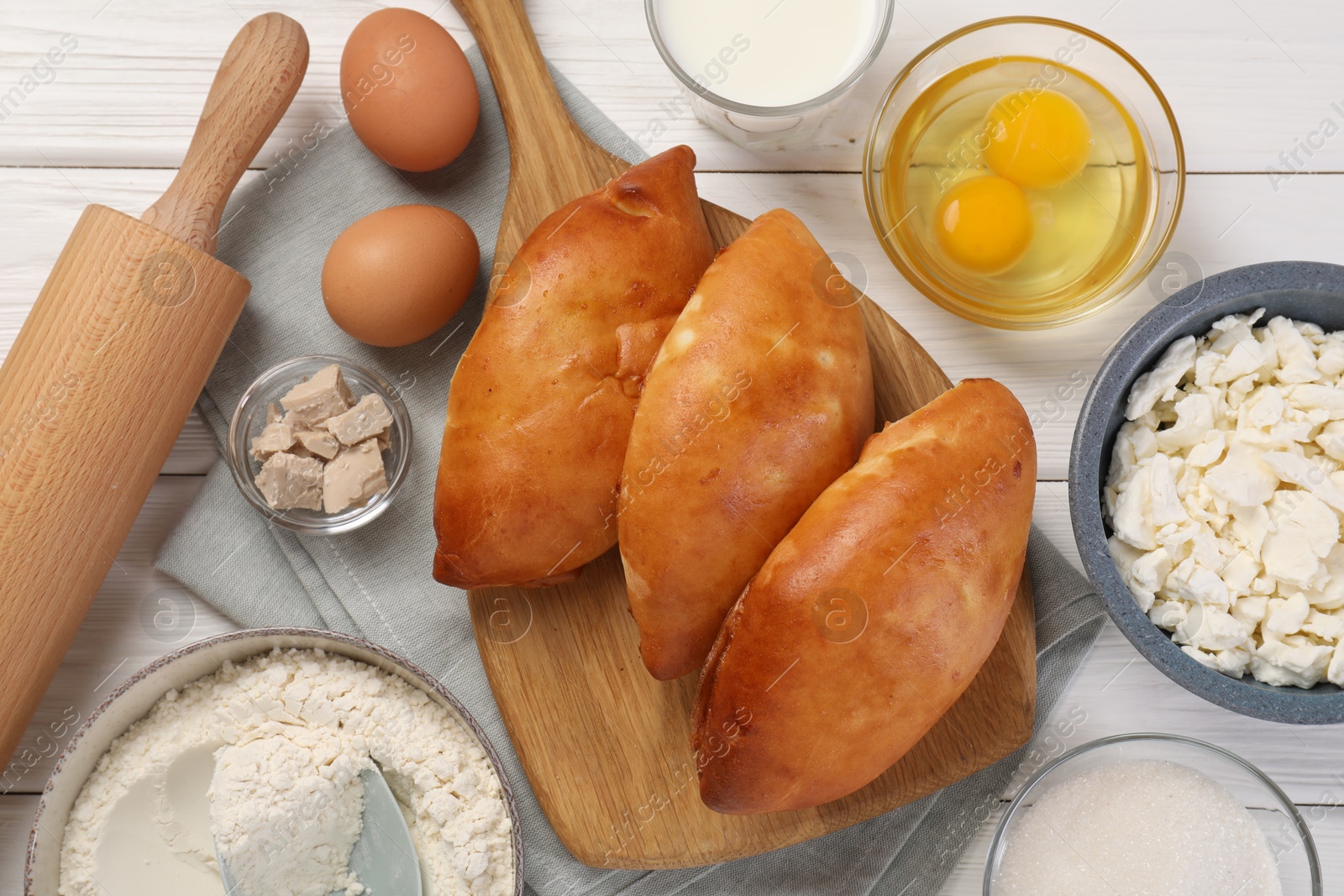 Photo of Delicious pirozhki (stuffed pastry pies) and ingredients on white wooden table, flat lay