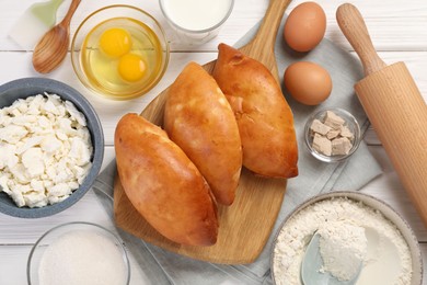 Photo of Delicious pirozhki (stuffed pastry pies) and ingredients on white wooden table, flat lay